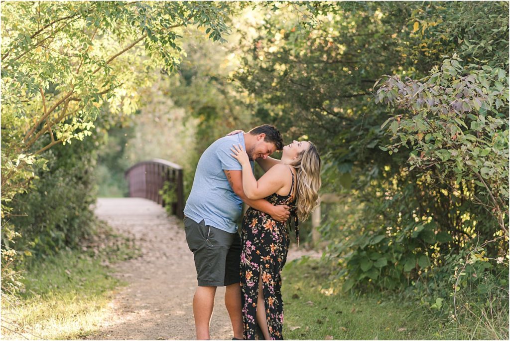 Engagement photo in Milford Mi of couple laughing in front of a pretty bridge on a nature trail.