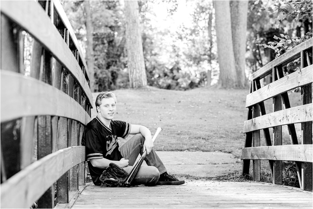 Boy sitting on a bridge in Downtown Milford, Mi in his baseball uniform. Senior Portrait.