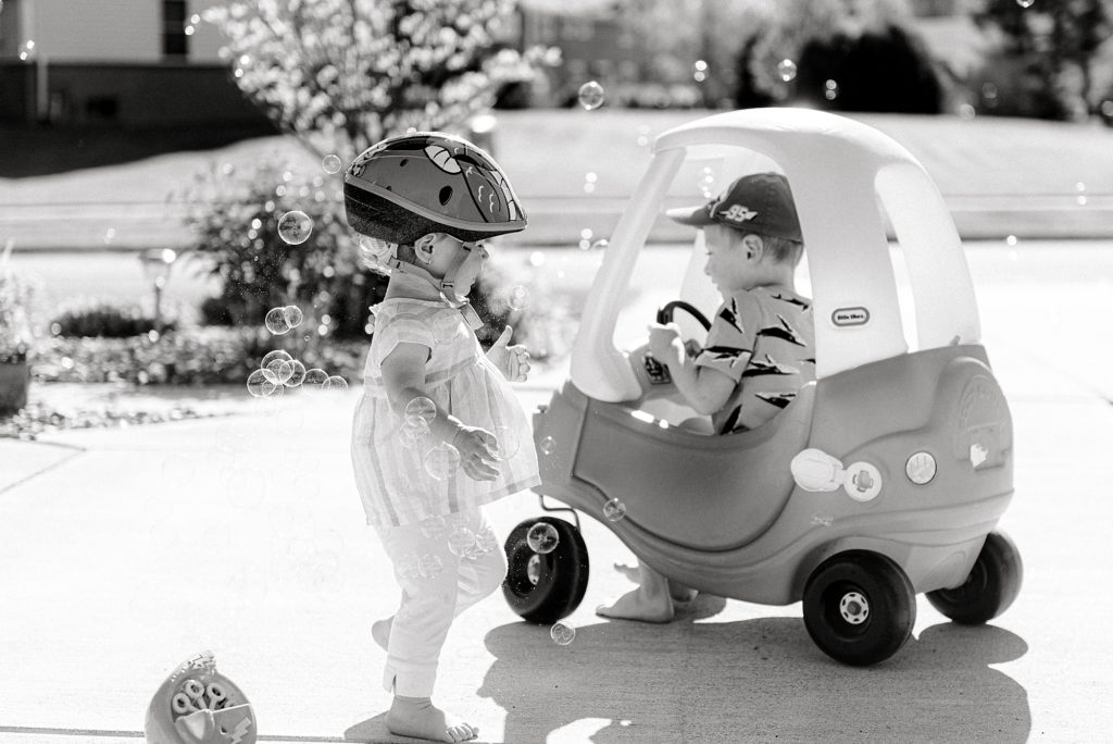 Black and white photo of children playing with a toy car and bubbles. Howell mi photographer life lately blog post.