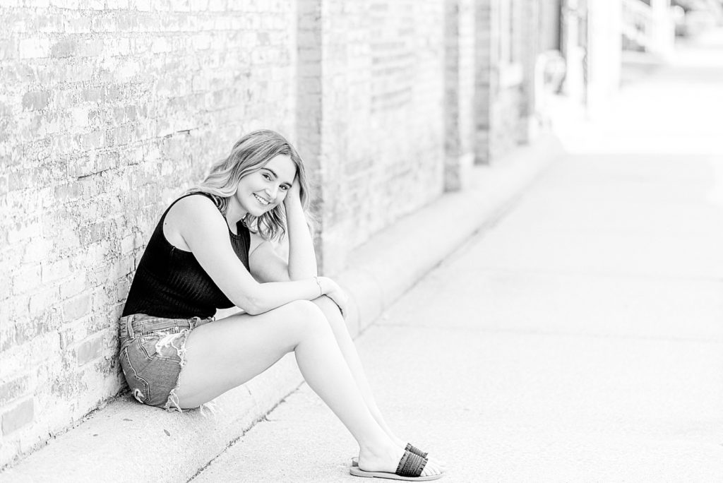 black and white photo of a girl sitting in front of a brick wall
