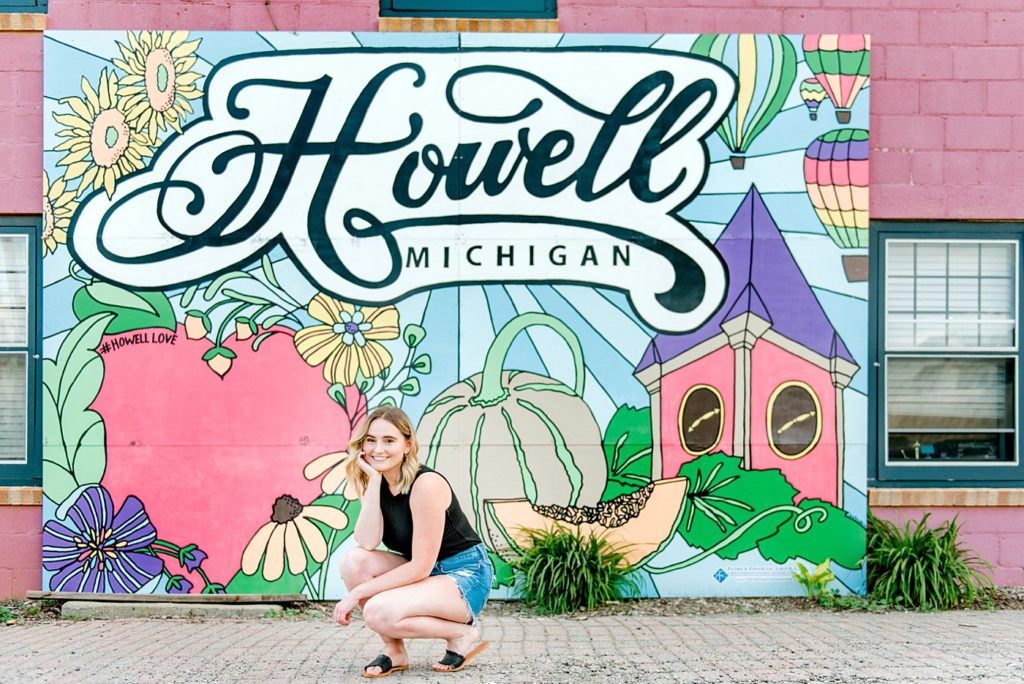 girl kneeling in front of a Howell Michigan sign in Downtown Howell