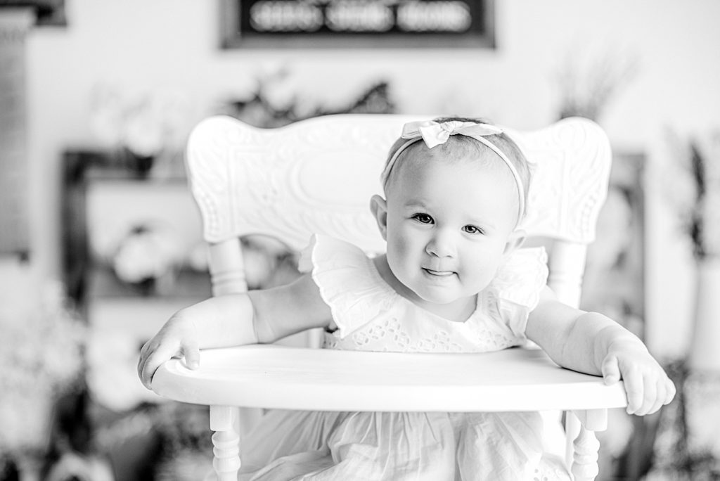 Baby in a pretty vintage white high chair in front of a floral backdrop for her first birthday photos and cake smash.