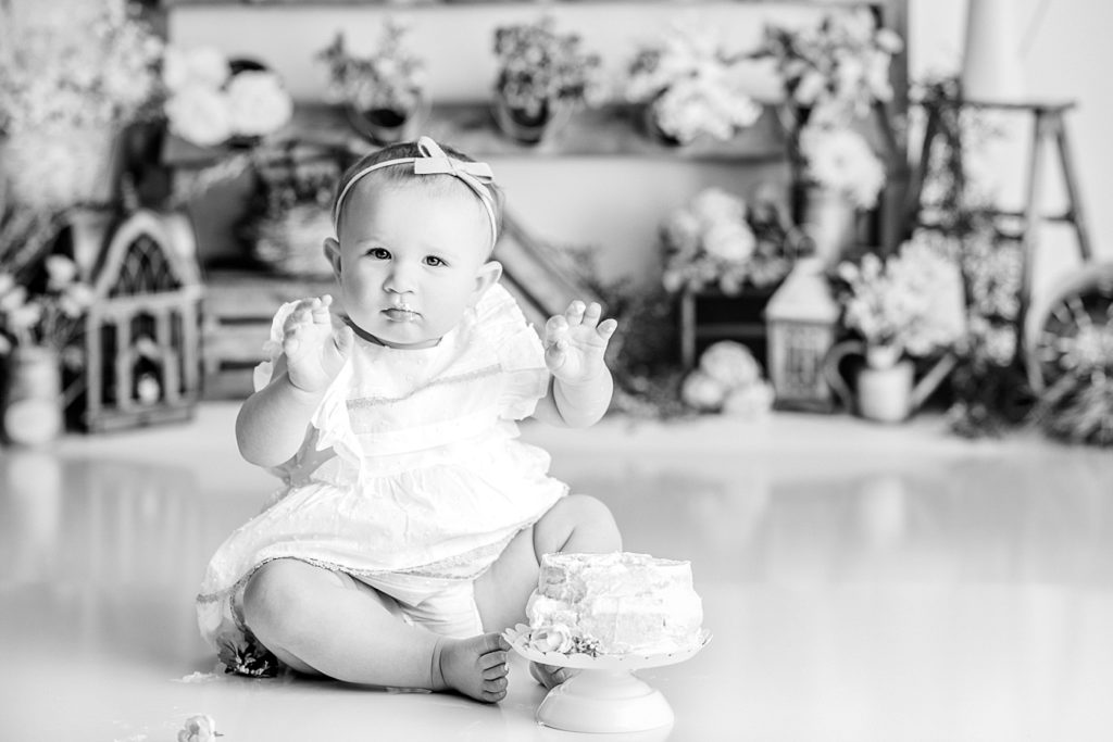 Black and White photo of baby eating cake at her first birthday floral cake smash photo shoot.