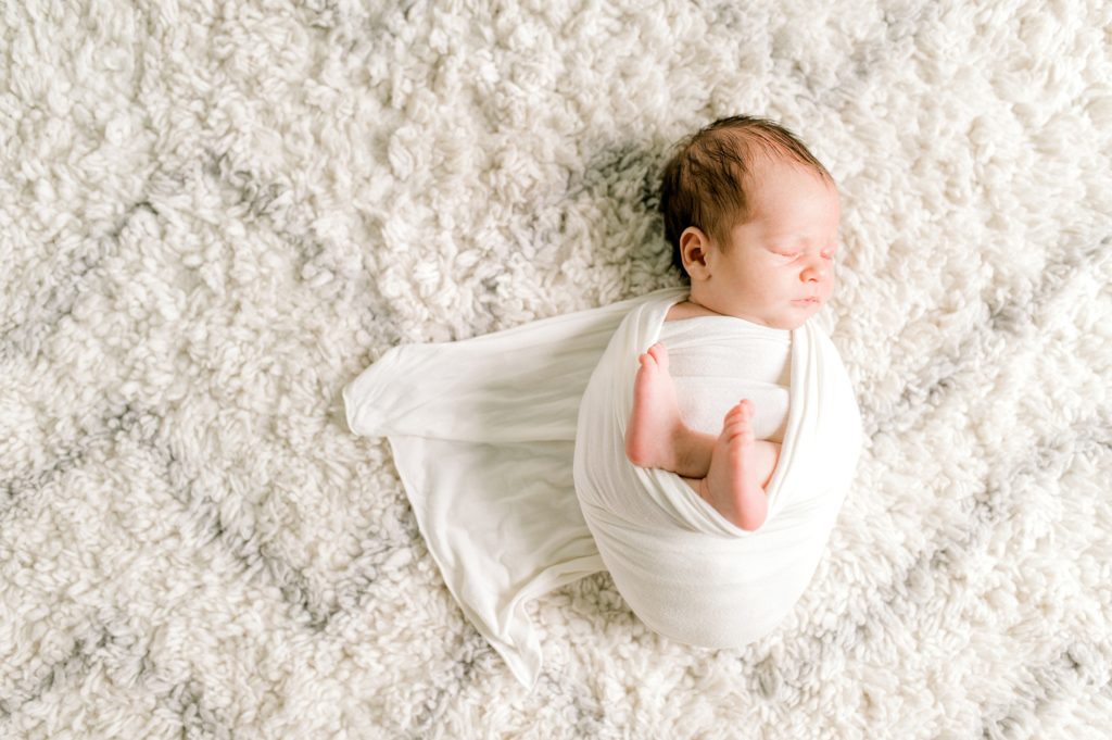 Newborn baby swaddled in a cream colored wrap.