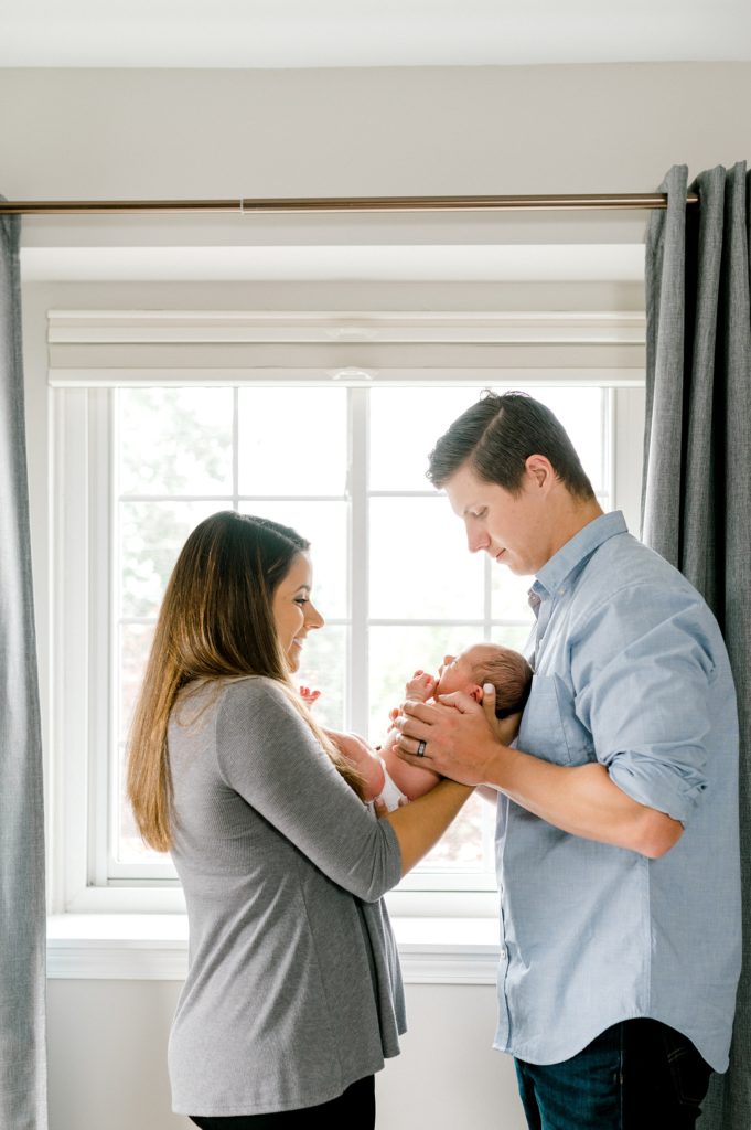 Silhouette of mom and dad with their newborn baby standing in front of a window.