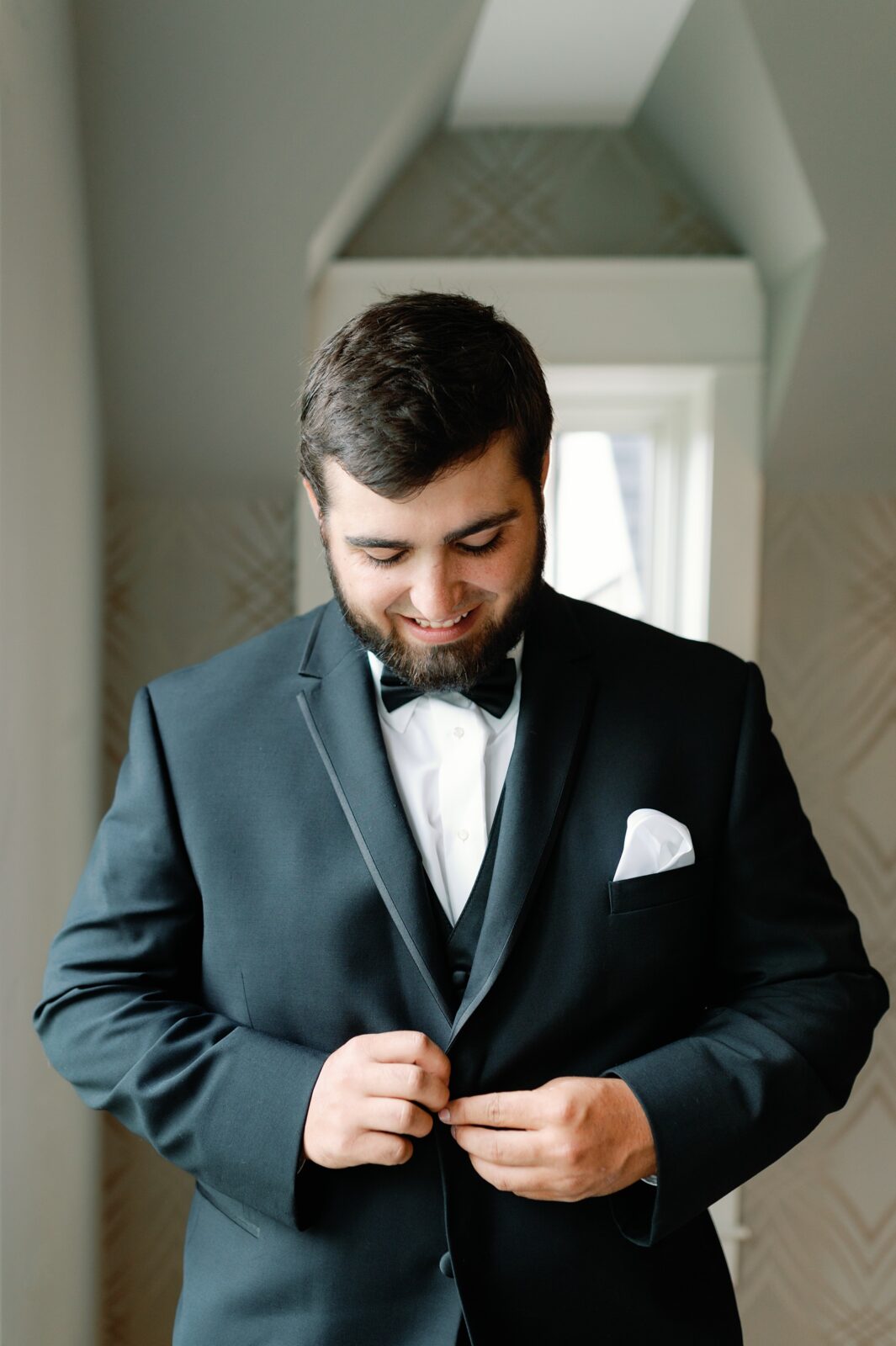 Groom smiling down as he button his suit jacket on his wedding day.