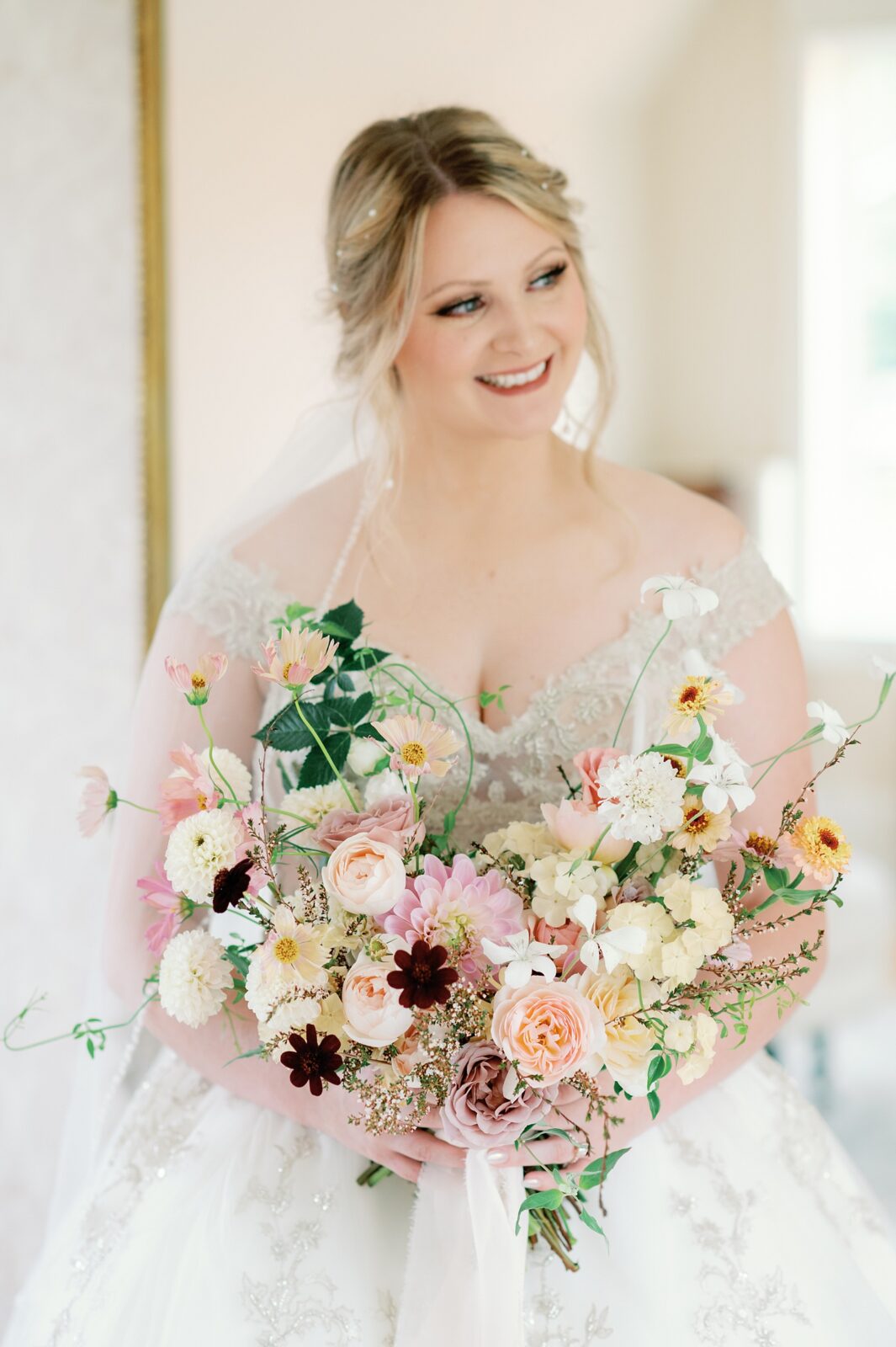 Bride smiling as she looks out the window at Venue 3Two in Grand Rapids, MI. Her bouquet is the focal point of the image, and is whimsical with spring colors.