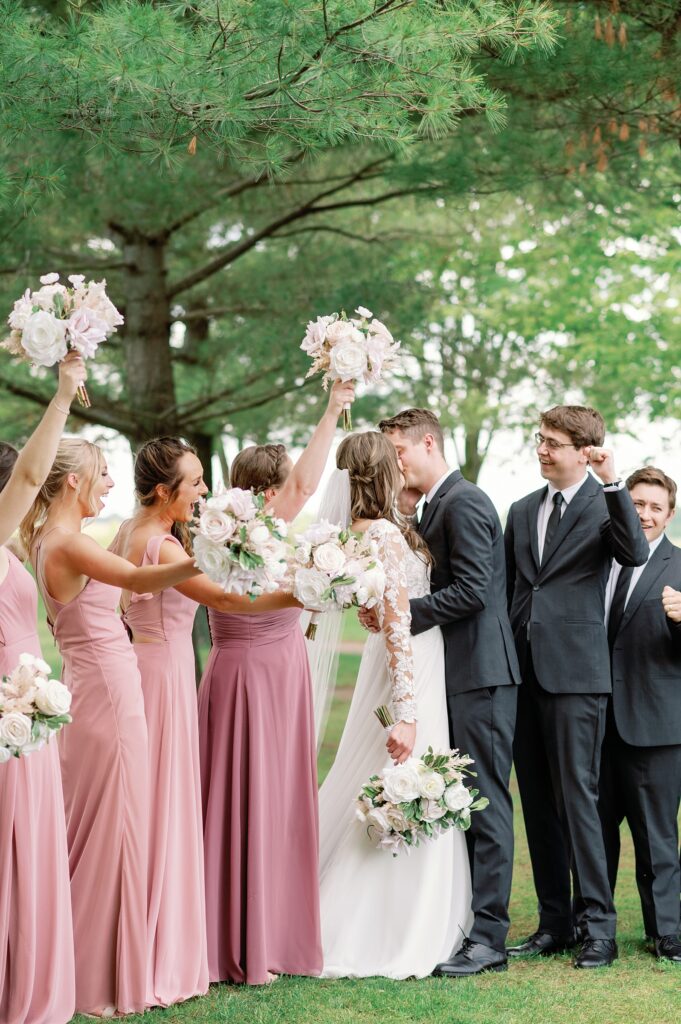 Bridal party cheering around the bride and groom as they kiss