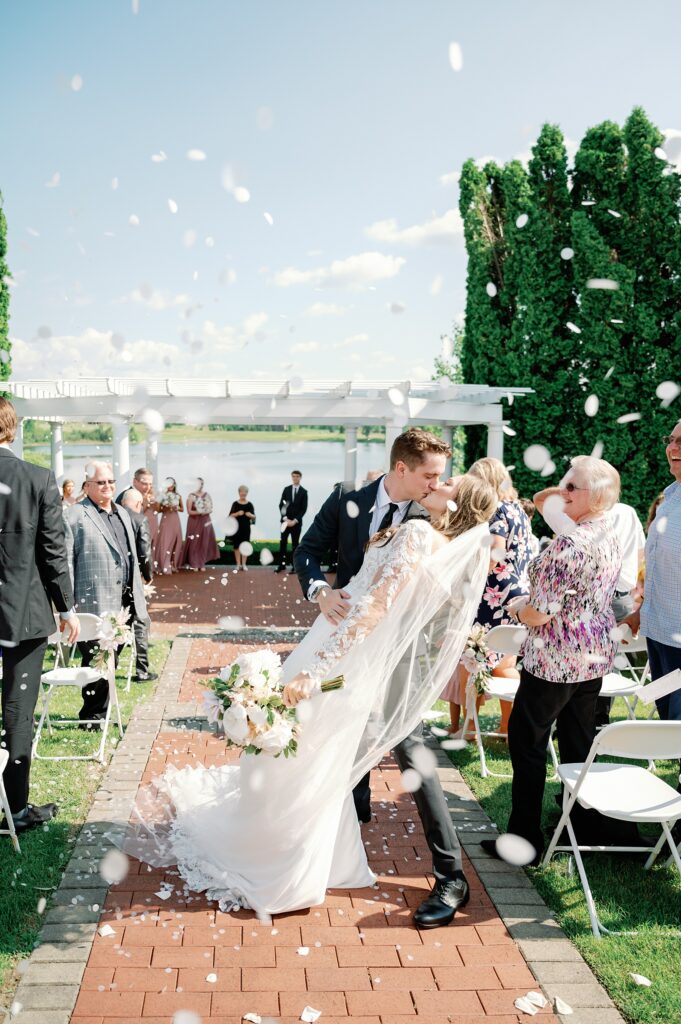 Bride and Groom kissing during the recessional among flower petals being tossed