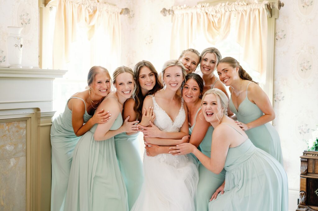 Bride standing in the getting ready space with her bridesmaids embracing in a group hug