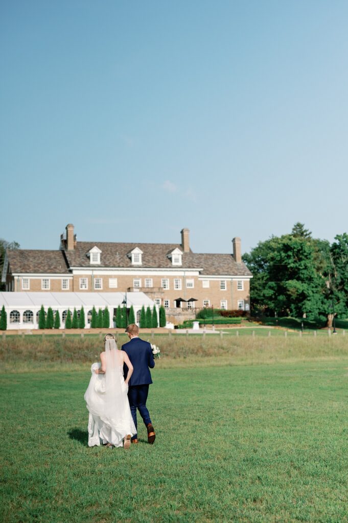 Bride and groom walking away from the camera with their wedding venue in the distance. The felt mansion.