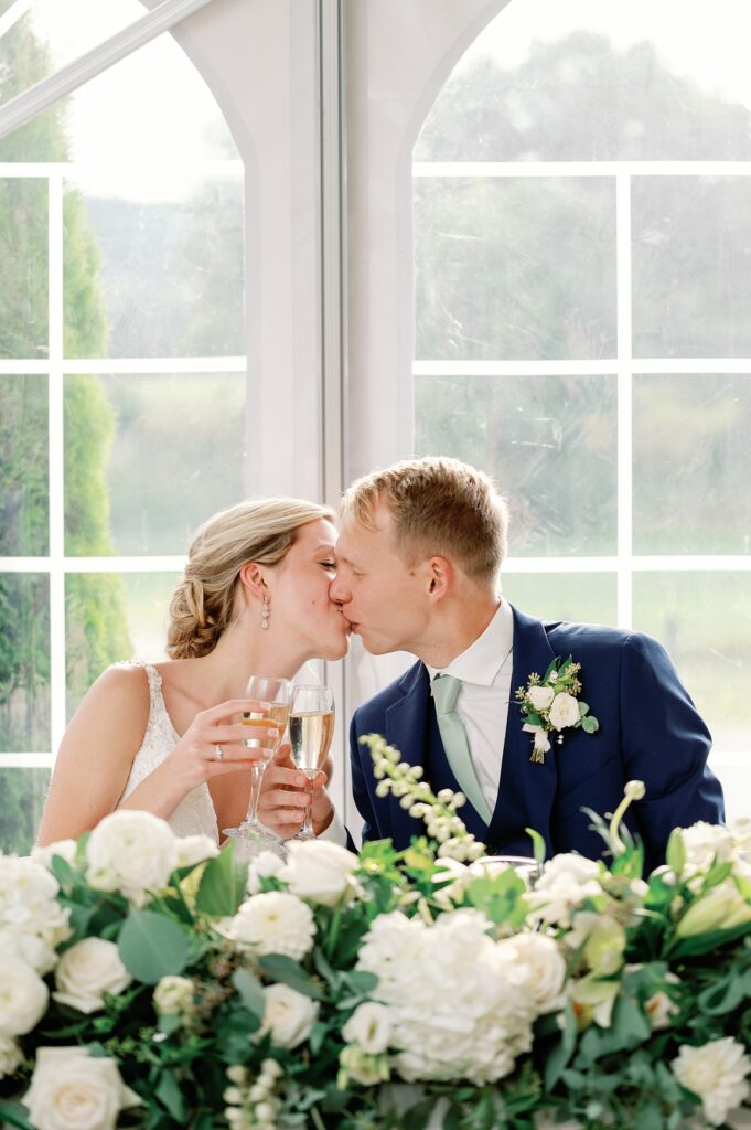 Bride and groom kissing at their wedding reception dinner table while toasting.