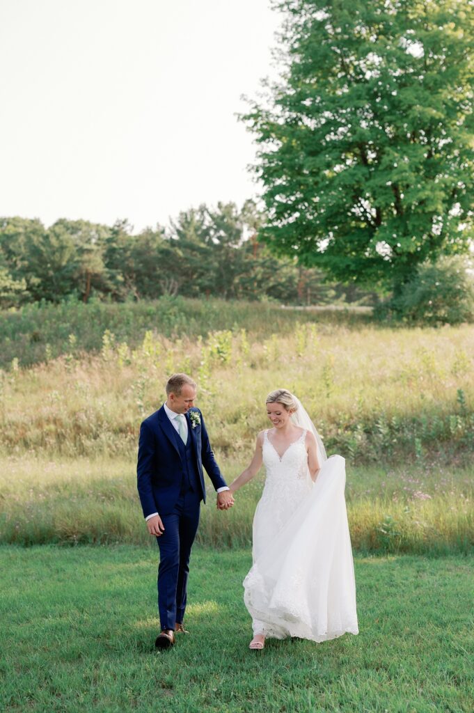 bride and groom walking together in front of a field. 